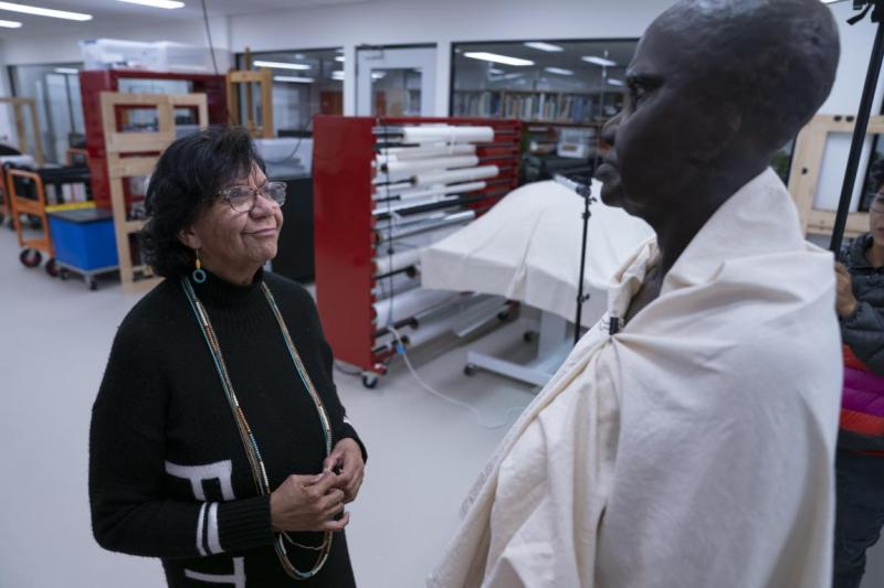 A woman looks at a life sized statue of a woman in robes