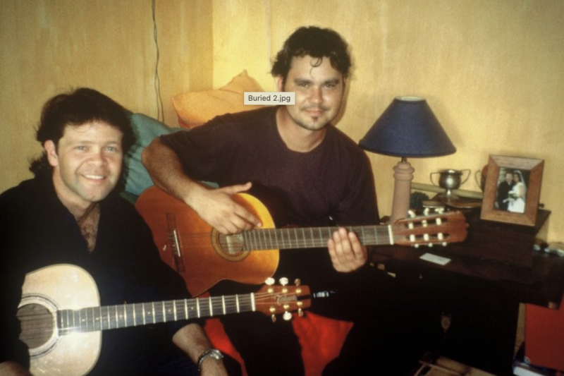 Two guitarists sit on a couch smiling