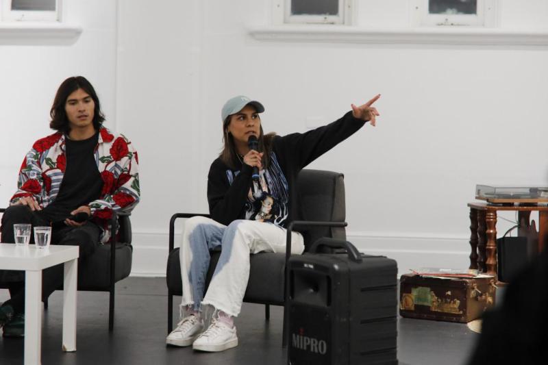 Ilona McGuire speaking into a microphone with arm raised during an artist talk